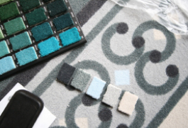 Detailfoto gewirkter Teppichelement-Muster. Die Farbabstufungen umfassen Grau-, Grün-, Blau- und Ockerabstufungen.