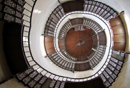 Photo with a dizzying view of the cantilevered spiral staircase of the observation tower running along the walls. It is made of cast iron. The openwork steps reveal the view into the depths.