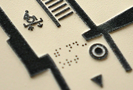 Detailaufnahme eines Schwelldruckes der taktilen Etagenübersicht. Zu sehen sind der Standpunkt mit dazugehörigem Braille-Schriftzug und das Rollstuhl Piktogramm.