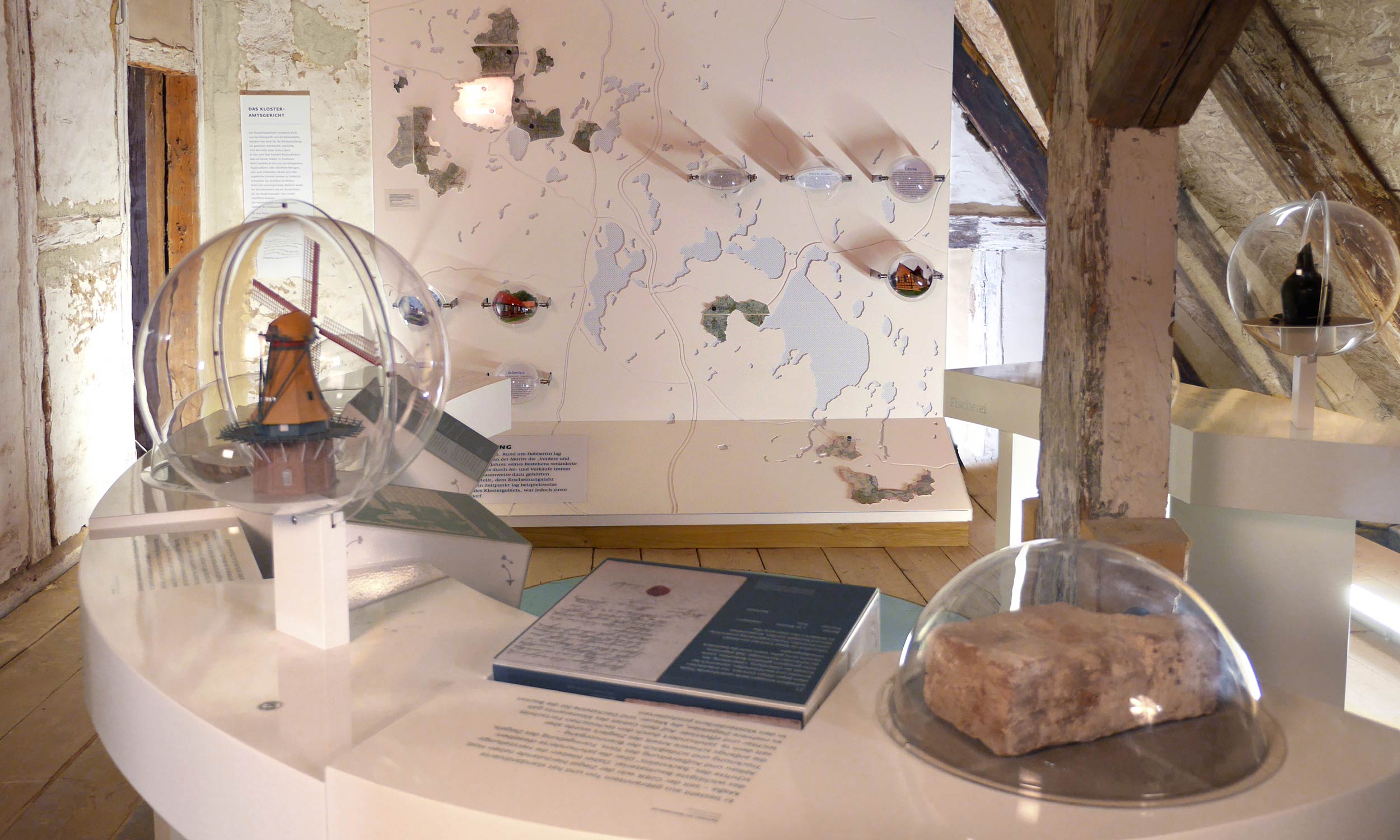 Foto des Ausstellungsraumes mit diversen Ausstellungselementen. Im Hintergrund eine Wandgroße Karte zu den Ausmaßen des Klosteramtes, im Vordergrund Tische mit den unterschiedlichen Wirtschaftszweigen.