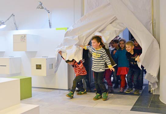 Opening of the experience space. Children stream through the entrance and break through the paper panels with which the entrance was covered before the entrance.