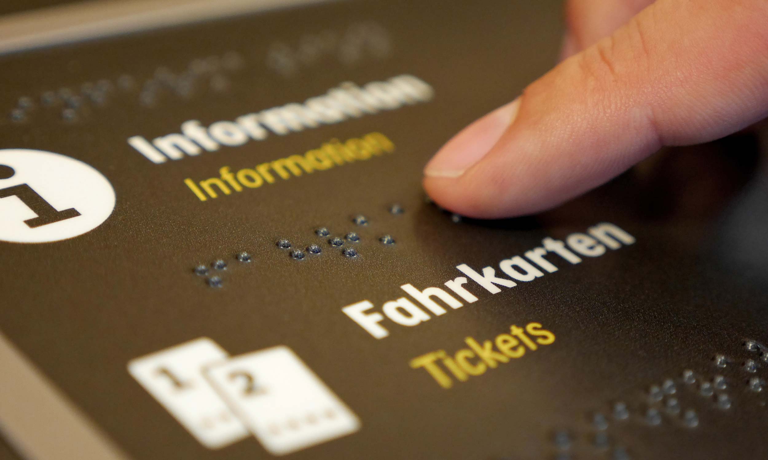 Detailfoto eines horizontal angeordneten Informationsschildes mit Braille