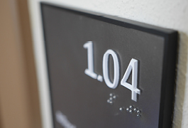 Detailfoto der Türbeschilderung sämtlicher Räume im Bürgerbahnhof: Gut zu erkennen sind die taktil ausgeführten Raumnummern in Braille und Profilschrift