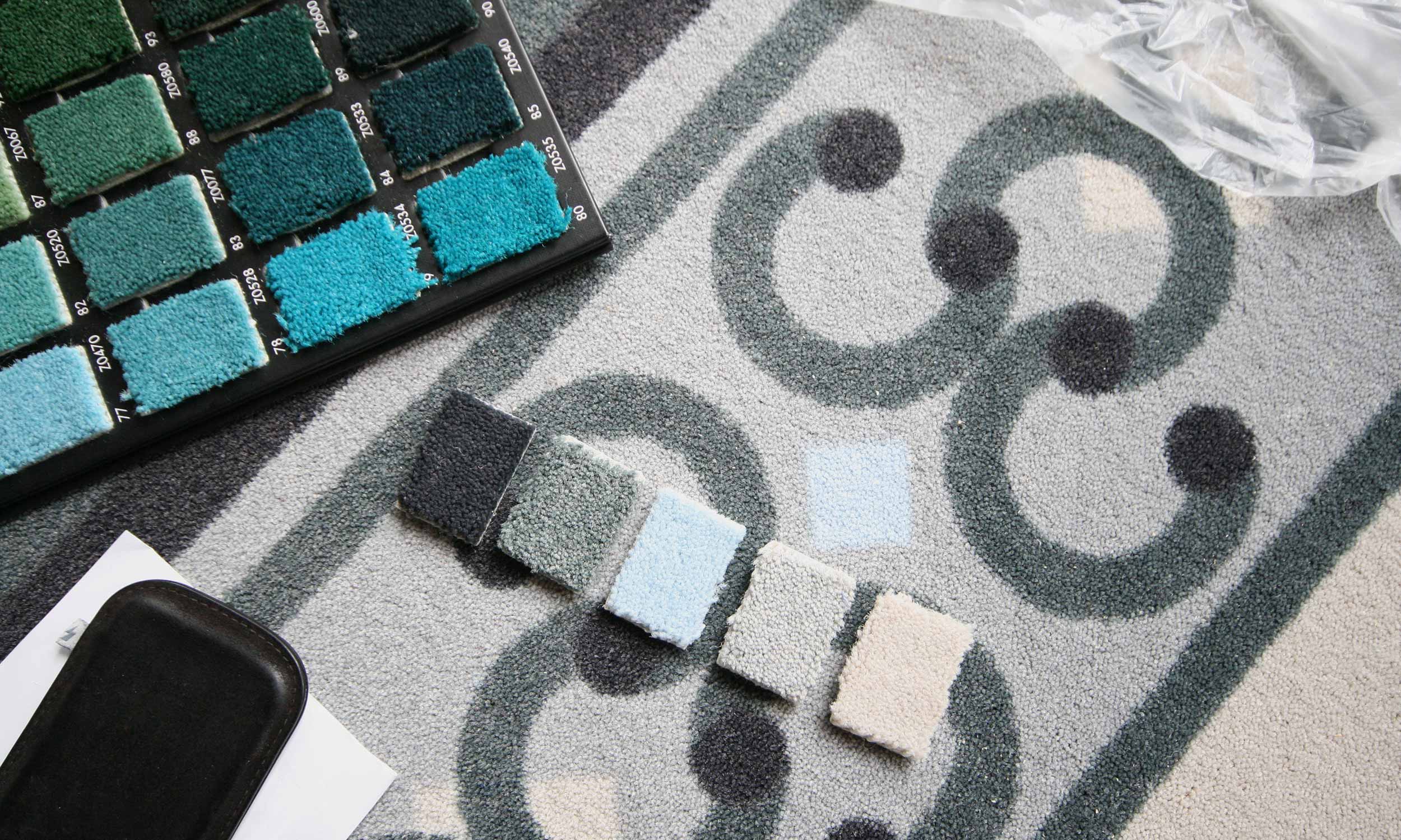 Detailfoto gewirkter Teppichelement-Muster. Die Farbabstufungen umfassen Grau-, Grün-, Blau- und Ockerabstufungen