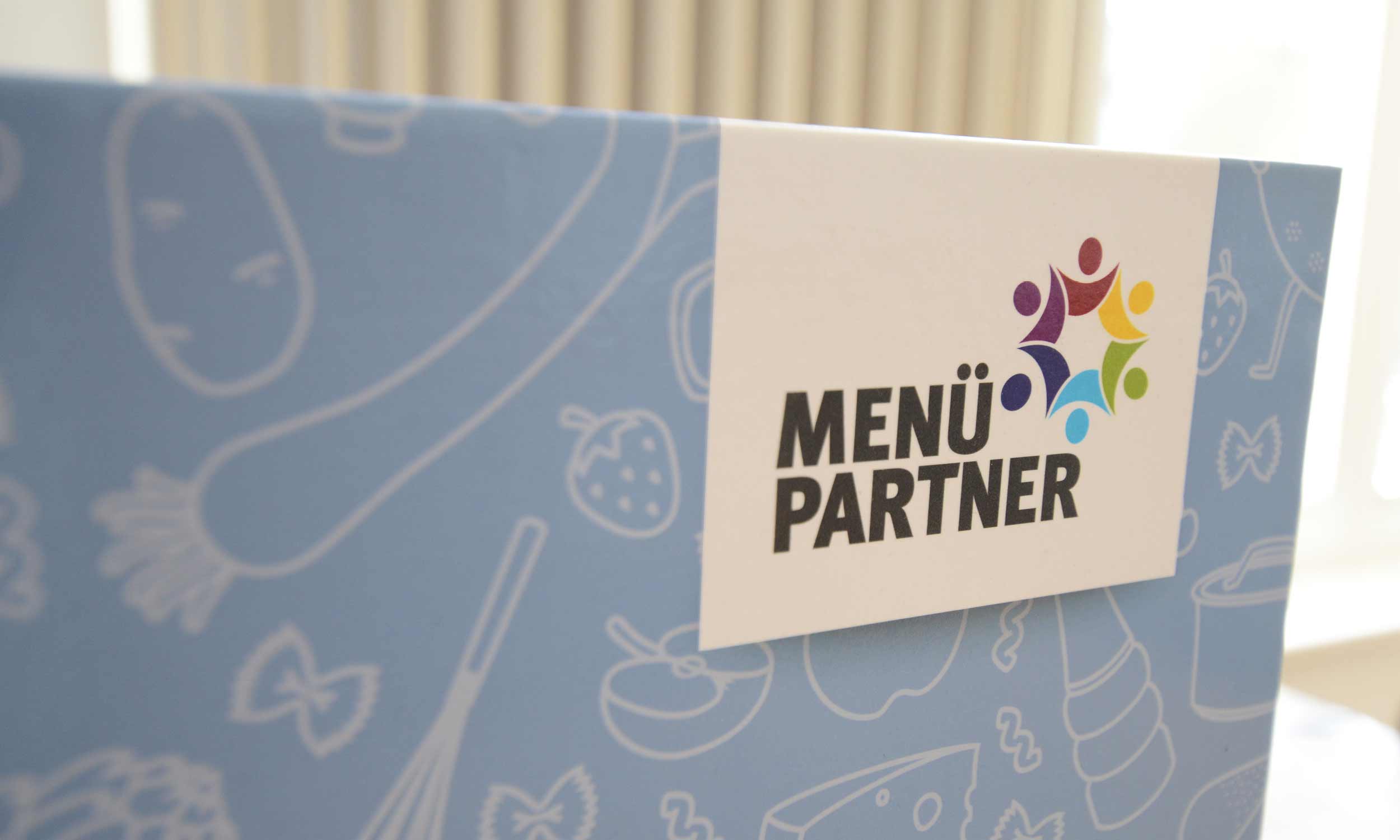 Photo of a designed menu partner ring binder with illustrative food items and the company logo.