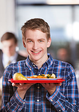 Foto eines Schülers, der mit beiden Händen ein Speisetablett mit Obst und Mittagsgericht hält