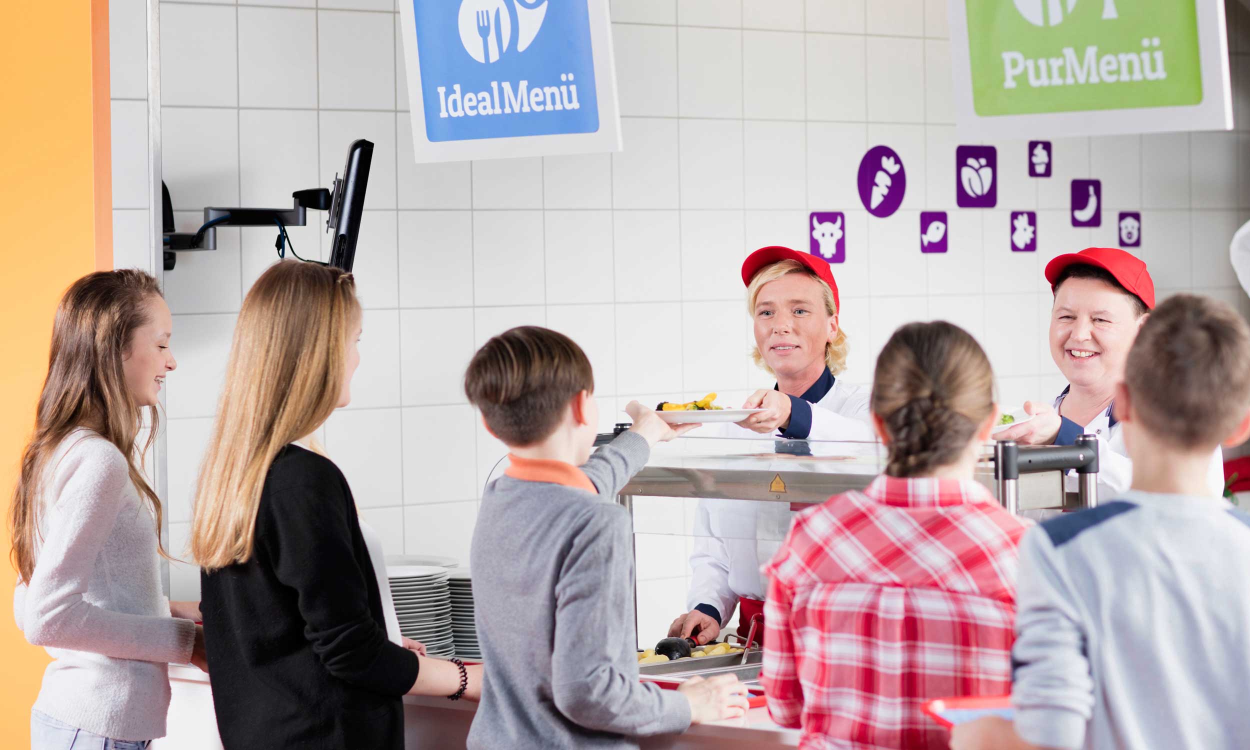 Foto einer modernen Menüpartner-Essensausgabe mit anstehenden Kindern und zwei Servierkräften hinter der Theke