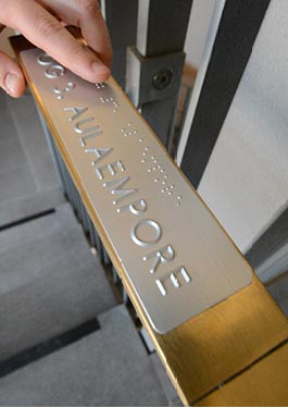 Close-up of a tactile handrail lettering with Braille and profile lettering. The finger of a person feels the Braille lettering.