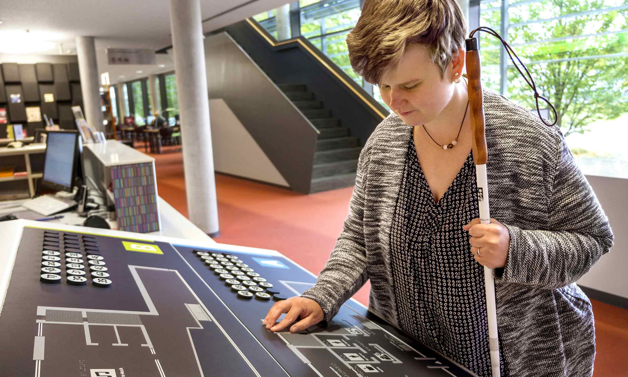 A blind young woman feels the tactile overview plans at the service counter of the State Library.