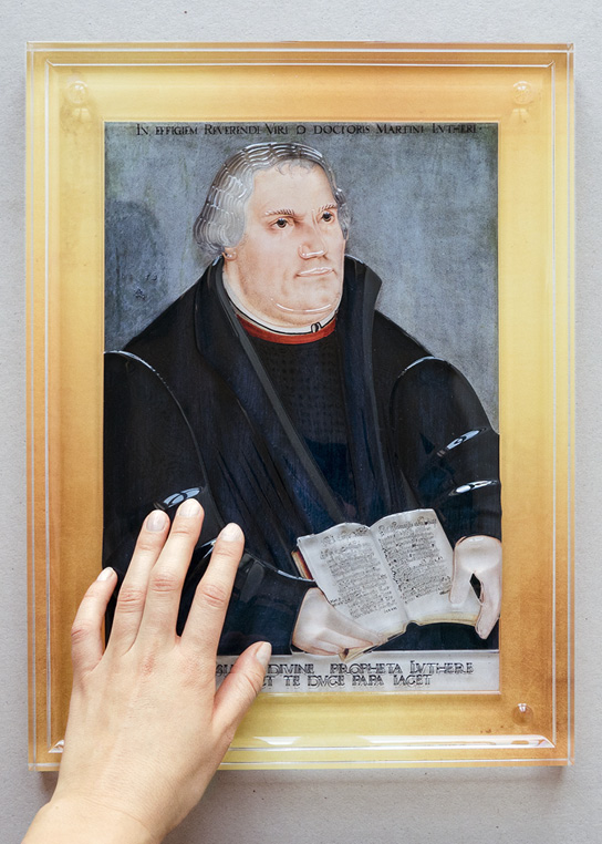 Foto des Tastgemäldes „Martin Luther“ von Lucas Cranach dem Jüngeren, das von einer Hand ertastet wird