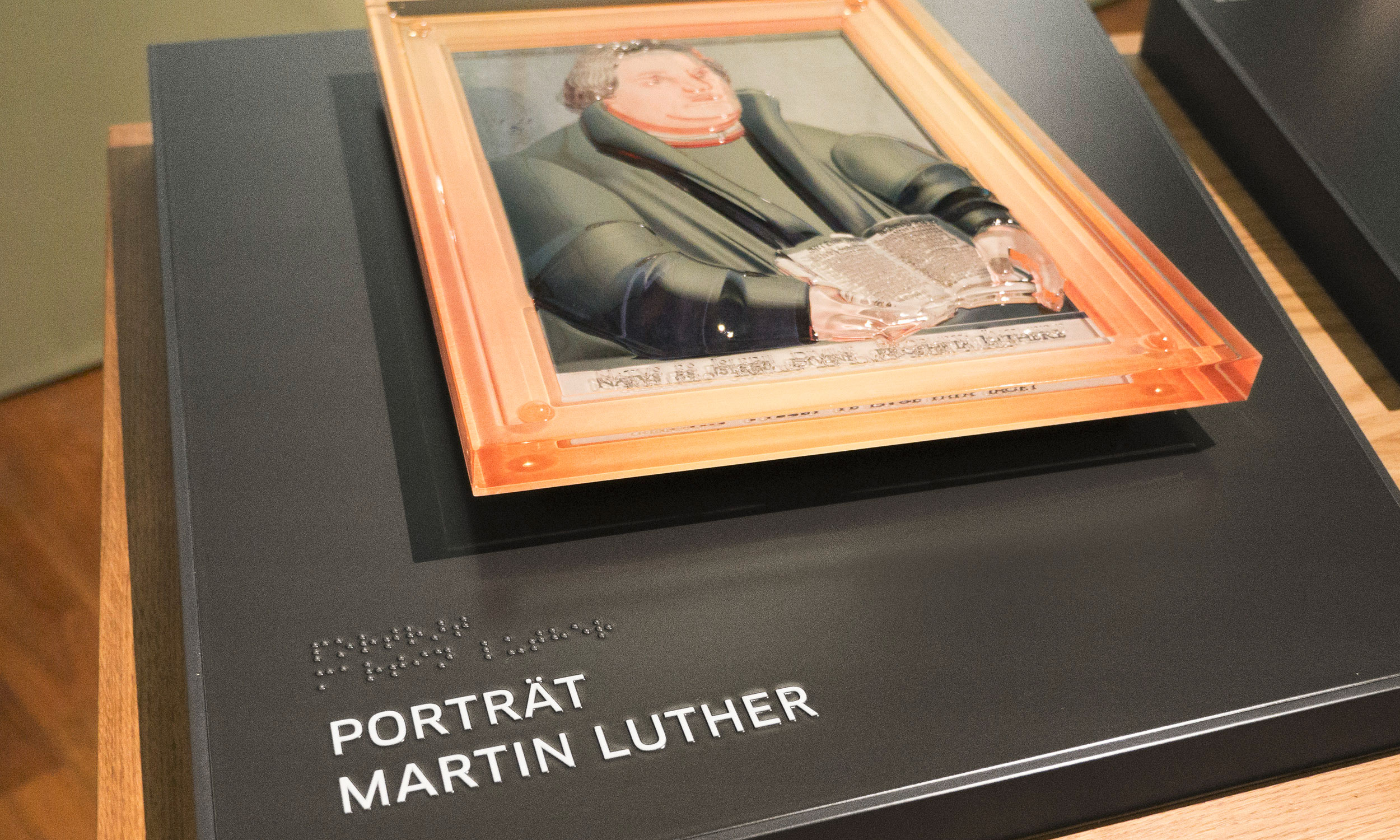 Detailfoto der Taststation mit drehbarem Luther-Gemälde auf einer Trägerplatte mit Beschriftungen in Braille und Profilschrift