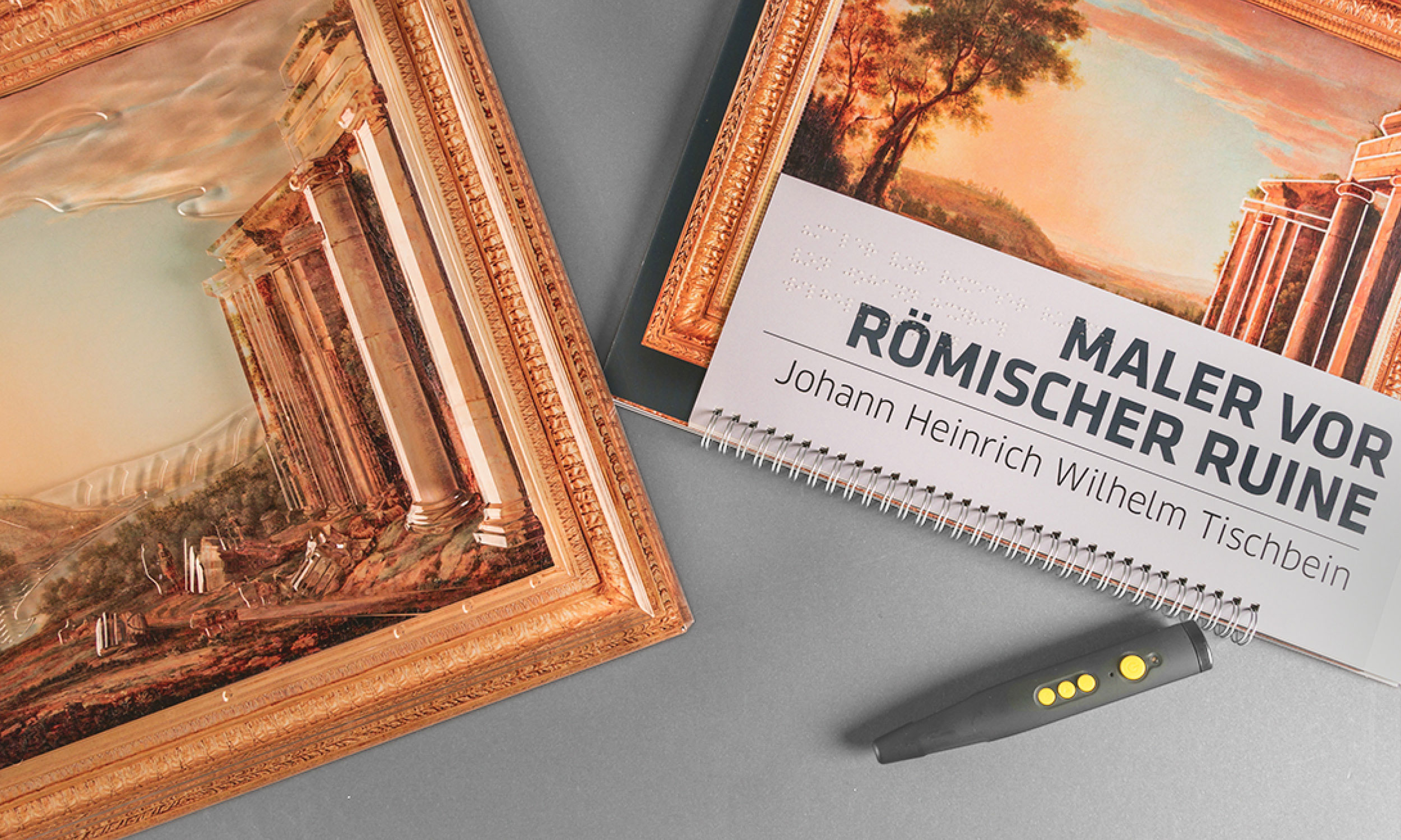 Photo of the touch painting and the tactile accompanying booklet "Painter in front of a Roman ruin" with enclosed hearing pen on grey table surface