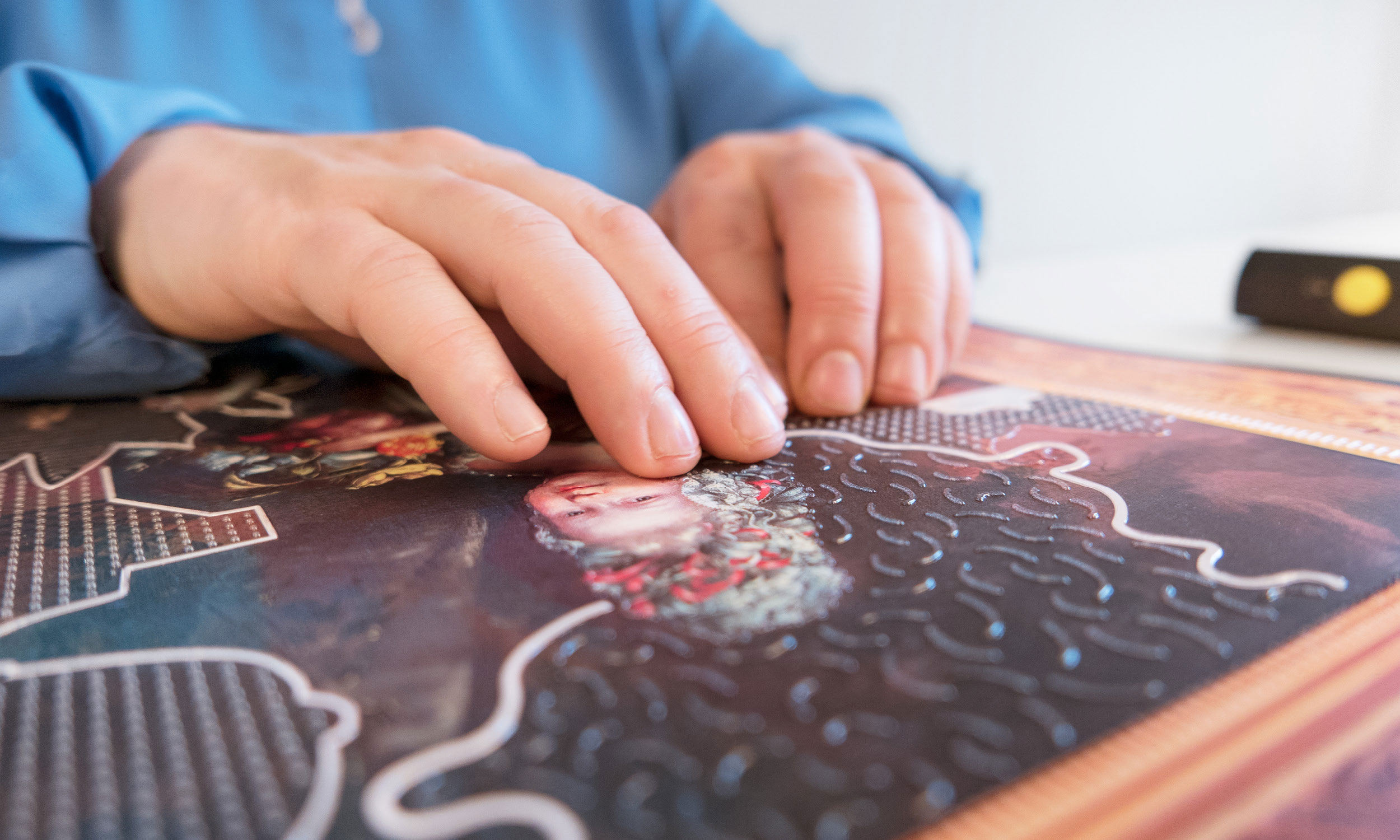 Detail photo of two hands scanning the surface of a tactile painting.