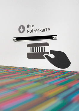 Close-up of the self-check-in; here the slot for entering the user card is marked by an infographic, below it the pattern with the coloured lines on a grey background.