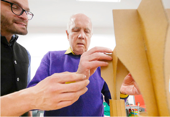 A blind man tries to grasp a cardboard model of the vault of St. Nicholas Church with the help of Gregor.
