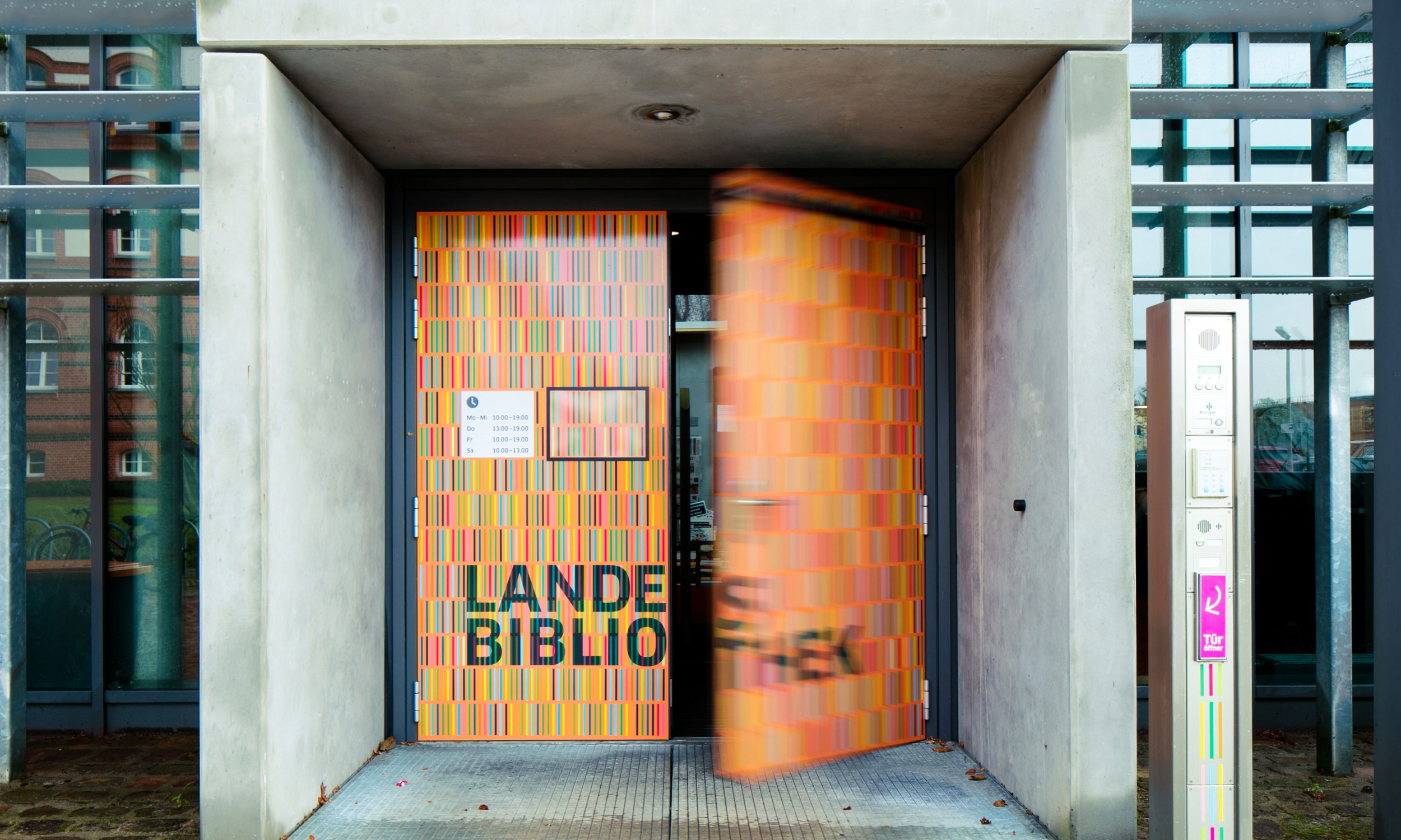 Foto der Haupteingangstür mit Beschriftung „Landesbibliothek“ und einer vollflächigen Gestaltung mit buntfarbigen Stäbchenelementen, die wichtiger Bestandteil der Leitsystems sind