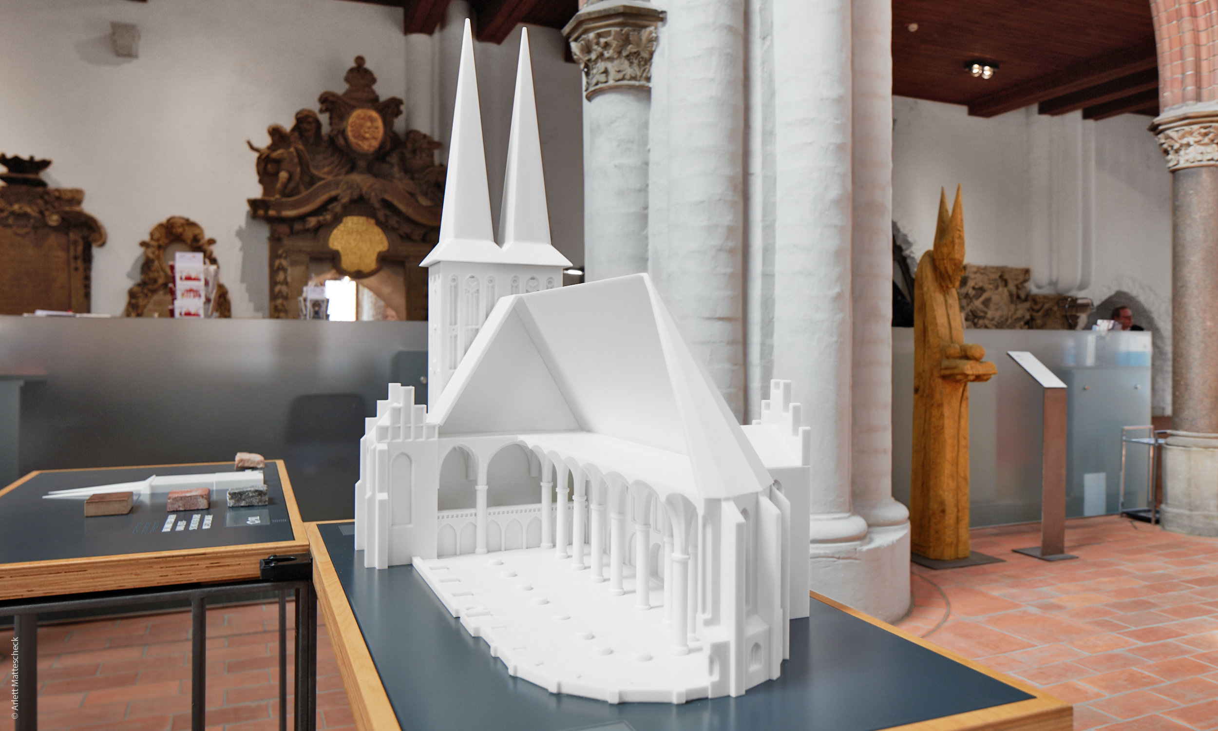 Dieses Foto zeigt die erste Station der Ausstellung von der Rückseite. Im Vordergrund befindet sich die Rückseite der Nikolaikirche, im Hintergrund befindet sich das Modell der Westfassade mit den Materialproben.