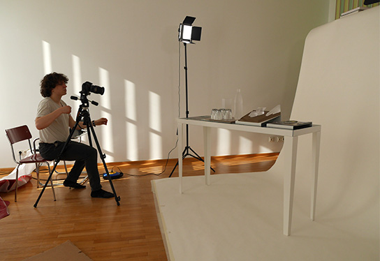 Auf dem Foto sieht man einen Mitarbeiter bei der Produktfotografie des Tastmodells „Gläserstilleben“ im Studio inkl.Design.
