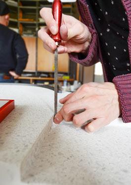 The photo shows two hands working on the base plate of a tactile model with a tool.