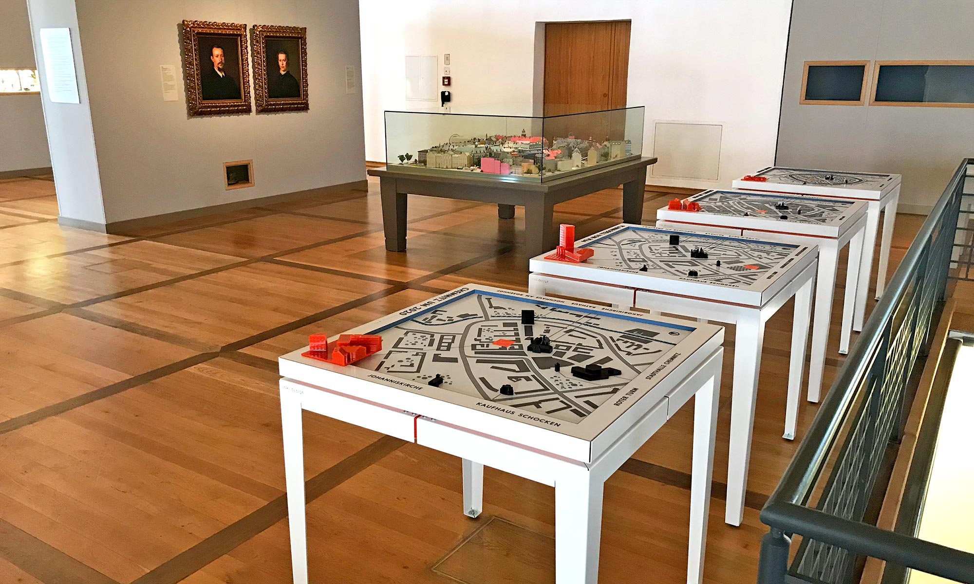 Ein Ausstellungsraume des Schlossbergmuseums in dem ein älteres Stadtmodell in einer großen Glasvitrine gezeigt wird. In unmittelbarer Nähe zu diesem Modell unter Glas die vier Tastmodelle von inkl.Design, die zum Anfassen einladen.