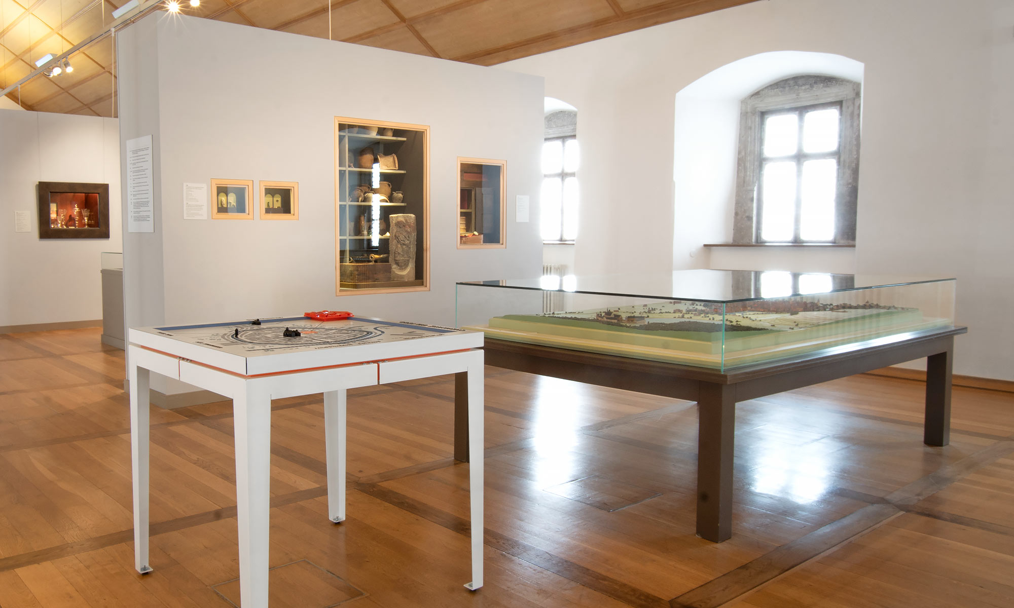 Blick in einen Ausstellungsraum, in dem eines der Tastmodelle und ein älteres Modell unter Glas nebeneinander stehen. Im Hintergrund weitere Ausstellungsstücke.