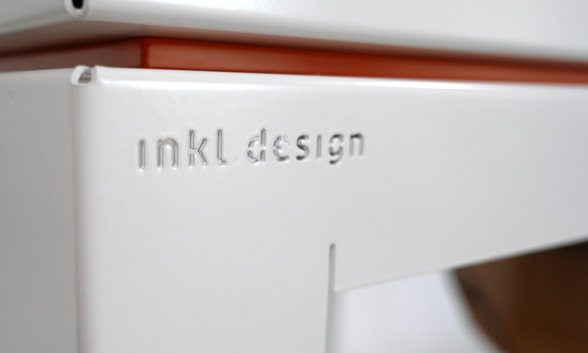 Detailaufnahme der Gravur „inkl. design“ auf dem weißen Tisch, der das Modell trägt.