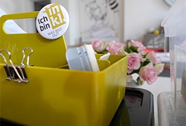 Eine gelbe Box mit Bürobedarf, an ihr hängt ein Ansteckbutton auf dem steht: „Ich bin inkl. Was bist du?“