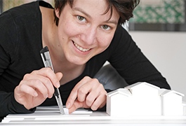 Franziska Müller from inkl.Design works on a model with a cutter knife and smiles into the camera.