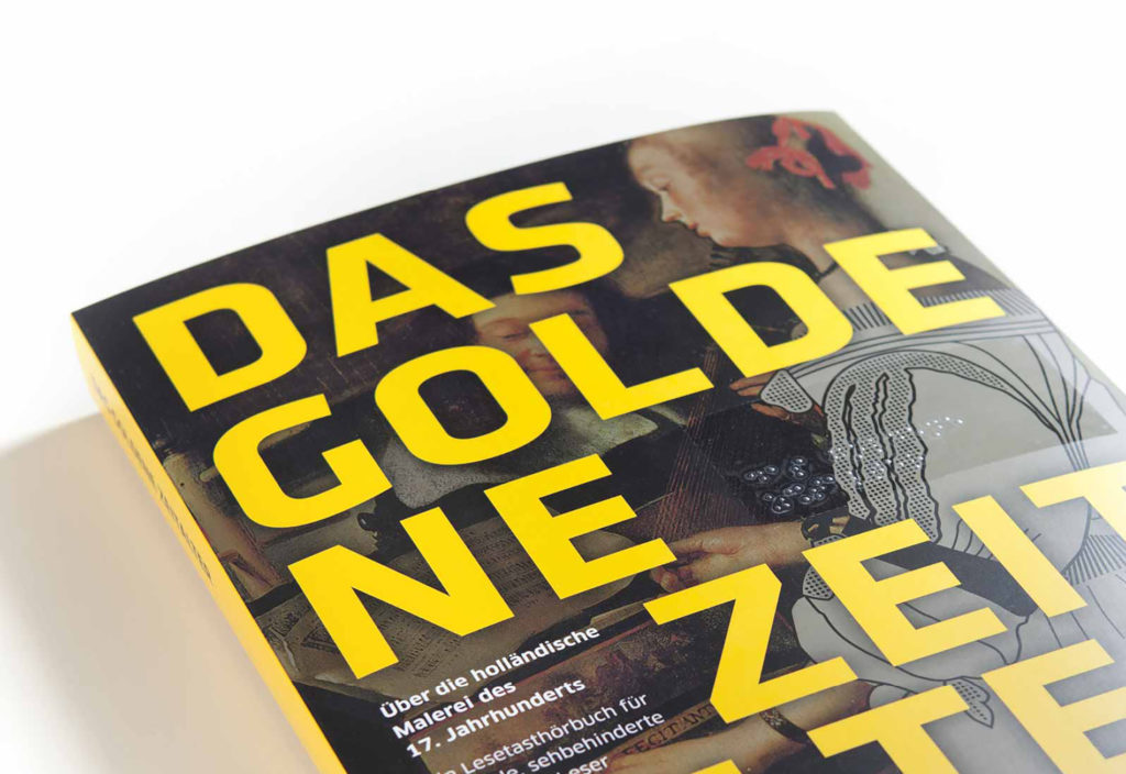 View of the title of the closed book lying on a white background. The title shows in the background, blurred and dark, a section of the painting „Dame am Cembalo“. On it, in large sunny yellow letters, the title of the book: The Golden Age, which is also applied in Braille with the help of a sticker.