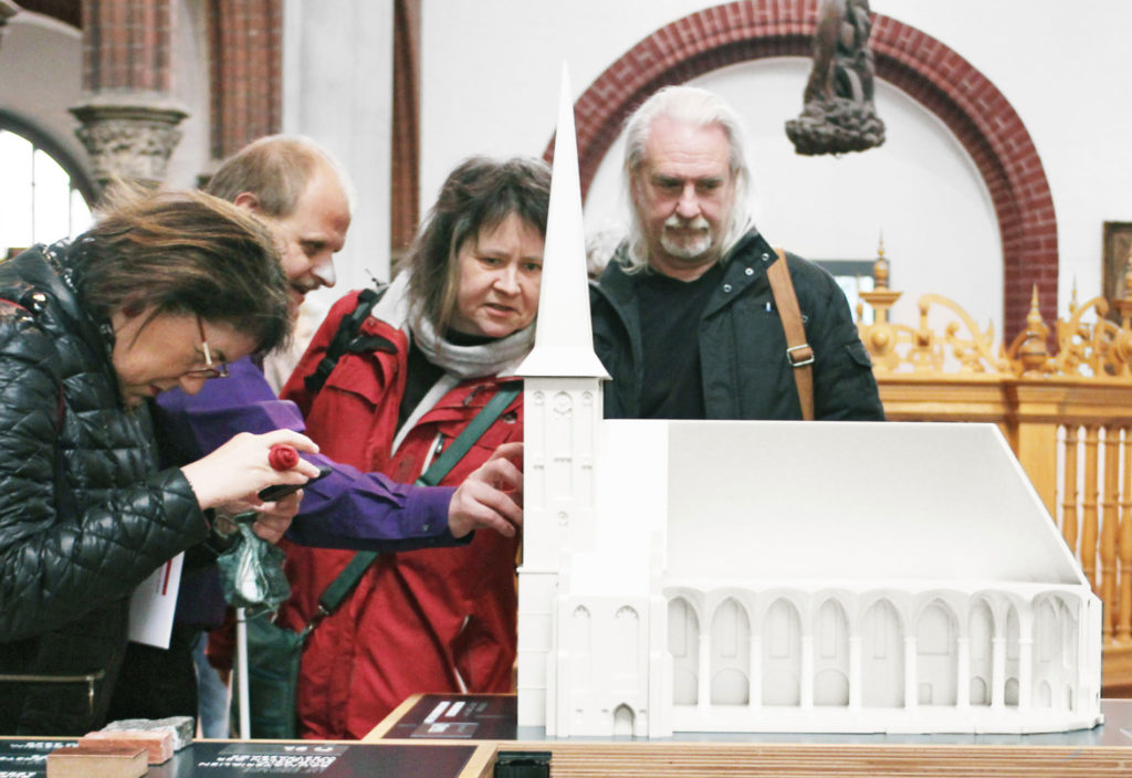 Auf dem Projektbild erkunden sehende und blinde Besucher und Besucherinnen das große Modell der Nikolaikirche.