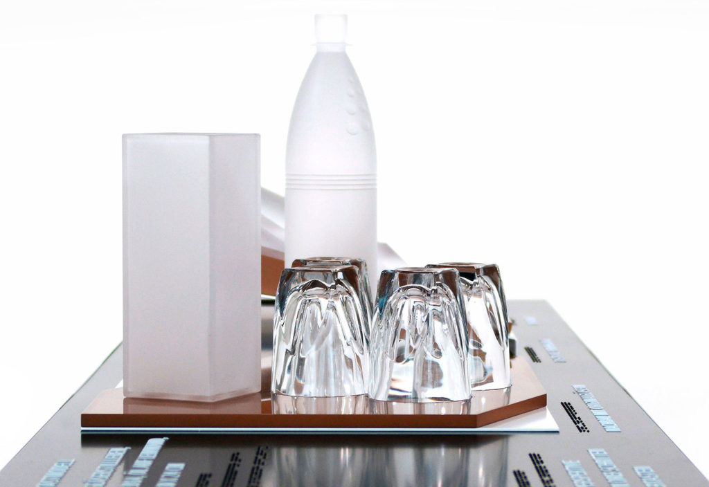 Titelbild für das Projekt "Perspektiven wechseln". Seitenansicht mit Gläsern und Flasche des taktilen Tastmodells „Gläserstillleben“ mit Blick auf die Halterung für Langstock und Unterarmstütze.