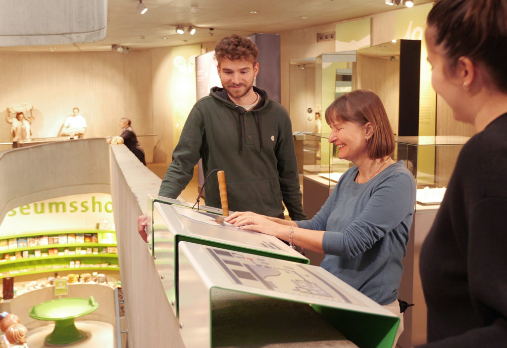 The project picture shows Till Henning and another employee of inkl.Design together with Tamara Ströter at a tactile model in the Neanderthal Museum.