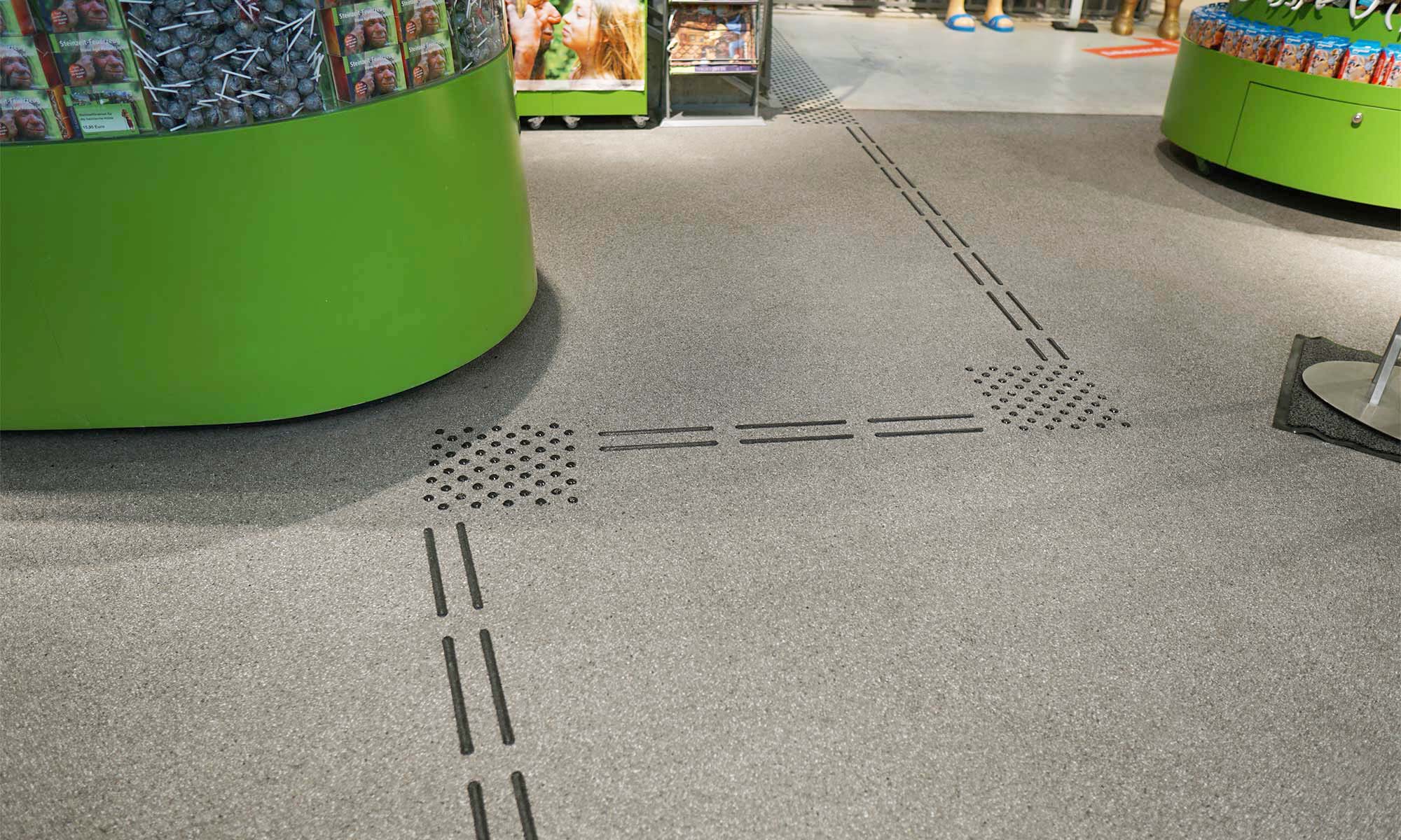 On the picture you can see floor indicators in the exit area of the museum. Paths are shown in this guidance system with two adjacent dashed black lines. These are interrupted by a square, black dotted area at the points where the path continues in a different direction.